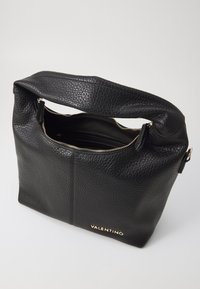 Svart läderhandväska med en texturerad yta, dragkedjestängning och guld "Valentino"-logotyp i botten. Enkel axelrem, minimalistisk design.