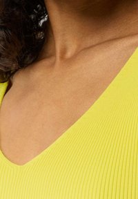 Gelber gerippter Stoff mit einem tiefen V-Ausschnitt-Design, das die glatte Textur und die sauberen Kanten zeigt, mit Fokus auf Schulter- und Schlüsselbeinbereich.