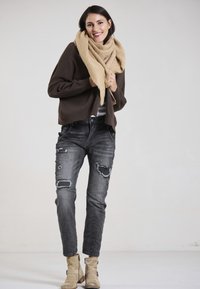 Brown knitted sweater, beige scarf, distressed black jeans with patches, beige ankle boots. Simple design, textured fabric, relaxed fit.