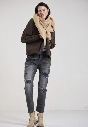Braun gestrickter Pullover, beiger Schal, ausgefranste schwarze Jeans mit Patches, beigefarbene Knöchelstiefel. Einfaches Design, strukturierter Stoff, lockere Passform.