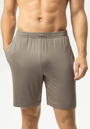 Mann trägt hellbraune elastische Shorts mit Taschen, gezeigt von der Taille bis zur Mitte des Oberschenkels, steht mit einer Hand in der Tasche.