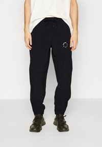 Marineblauwe sweatpants met elastische boorden en een trekkoord in de taille. Bevat een ronde witte logo op de linkerdij. Lichtgewicht stof.
