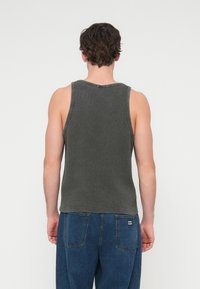 Γκρι βαμβακερό τοπ με ριμπ υφή, με στρογγυλή λαιμόκοψη και φαρδιές μασχάλες, που φοριέται με μπλε τζιν παντελόνι.