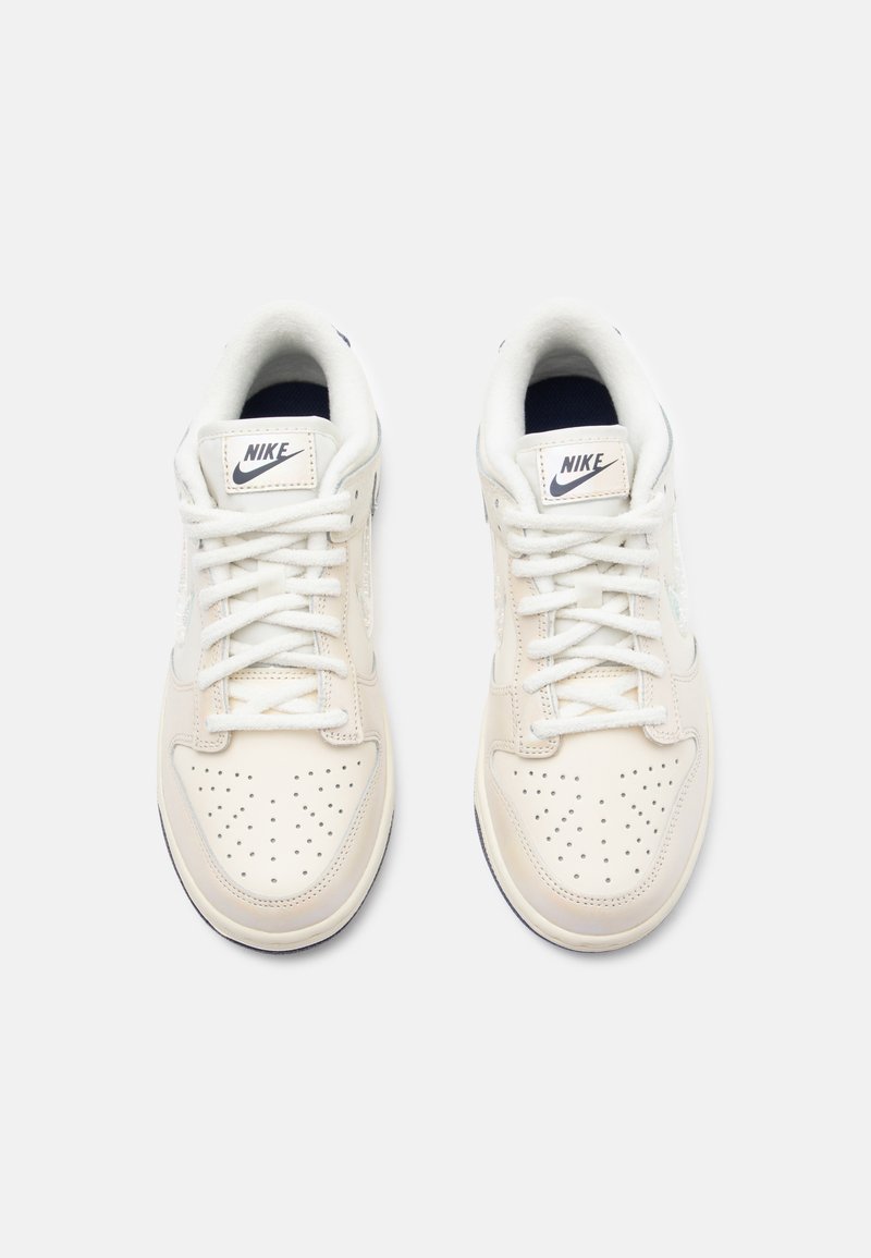 Sneaker Nike con tomaia in pelle crema, puntale perforato, lacci bianchi e accenti blu navy a contrasto sulla linguetta e foderato interno.