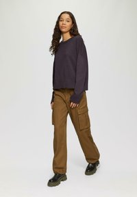 Oversized donkerpaars sweater met geribde manchetten en zoom, gecombineerd met bruine cargobroeken met grote zijzakken. Zwarte chunky laarzen maken de look compleet.