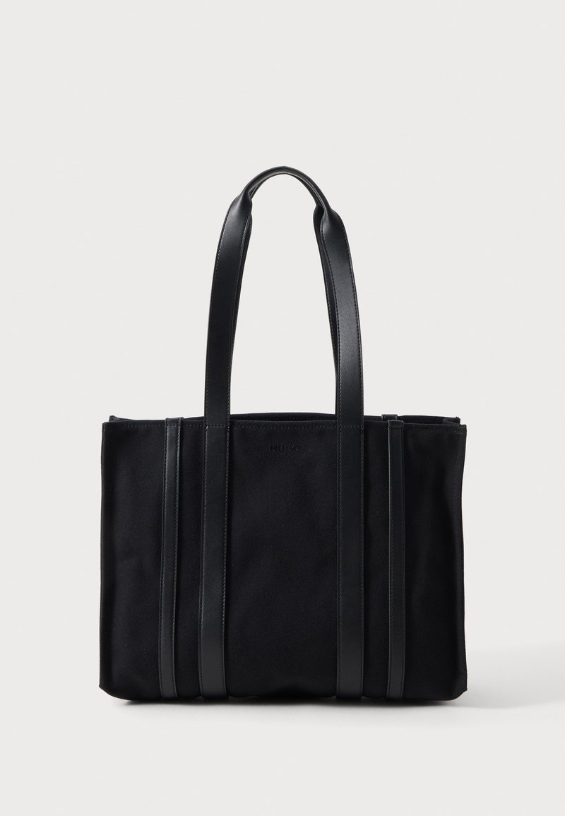 Sac cabas rectangulaire noir avec deux longues anses et des accents en cuir verticaux à l'avant, sur un fond clair uni.