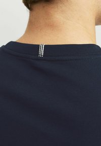 Navig blå bomullströja med rundad halsringning, med en vit trådaccent nära halsen och slät textur.