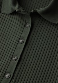 Polo shirt a coste verde scuro con colletto e sei bottoni neri lungo la pattina, con una finitura in tessuto testurizzato.