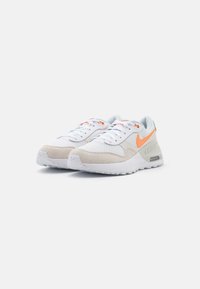 Weiße Sportschuhe mit strukturiertem Mesh-Obermaterial, Wildlederakzenten, orangefarbenem Nike-Logo und sichtbarer Luftpolsterung in der Ferse, ausgestattet mit einer weißen Sohle.