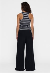 Pantaloni a gamba larga neri abbinati a una canotta a righe bianco e nera, con design a schiena scoperta. Tessuto morbido con una vestibilità comoda.