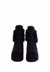 Stivaletti neri alla caviglia in suede con colletto in finta pelliccia, caratterizzati da un design con lacci e suole spesse. Accenti testurizzati sulla parte superiore.