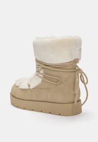 Bottines en faux suède beige avec un col en fausse fourrure crème, des lacets sur le côté et une semelle en caoutchouc. Texture douce et forme arrondie avec un aspect rembourré.