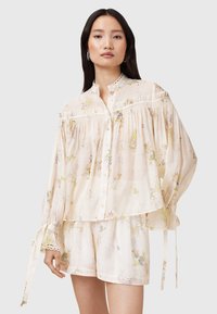 Lightweight floral blouse in cream with billowy sleeves and button closure, featuring lace trim and gathered detailing. Paired with matching shorts.