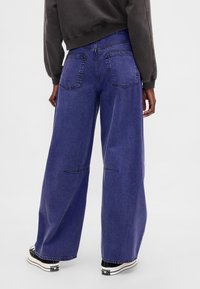 Ohlapne, široke kavbojke z visokim pasom, modrega jeansa, z dvema zadnjima žepoma in vidnimi šivi, kombinirane s črno-belimi supergami.