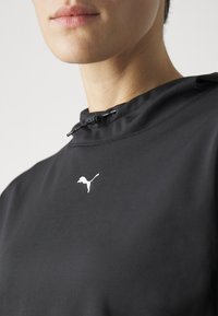Sudadera con capucha negra con un alto cuello, ajuste de cordón y un logo blanco de Puma en el pecho. Tejido suave y ligero.