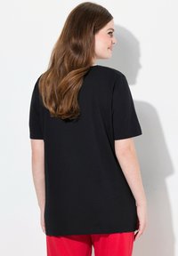 Zwarte katoenen t-shirt met korte mouwen, relaxte pasvorm en ronde hals, gecombineerd met rode broek. Duidelijke textuur en effen kleur.