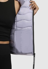 Light purple puffer jacket with a quilted interior, featuring a zip closure and interior pocket, shown being held open.