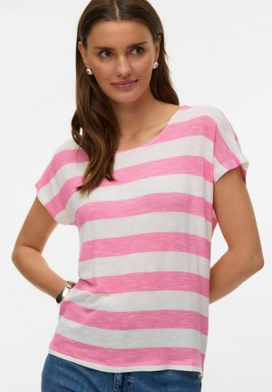 Femme portant un haut à manches courtes à rayures horizontales roses et blanches, un jean bleu, des boucles d'oreilles en perles et une montre-bracelet, posant avec la main sur la hanche.