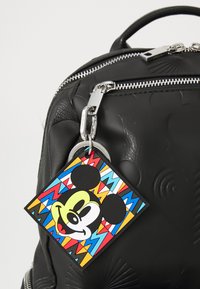 Zaino in pelle nera con texture embossata, cerniera argento e un portachiavi di Topolino colorato con motivi geometrici.