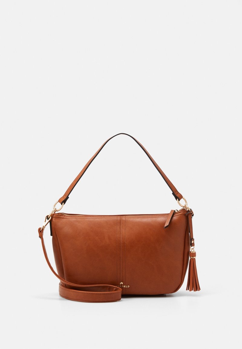 Sac à main en cuir marron avec poignées supérieures, bandoulière amovible, quincaillerie dorée et détail pompon sur fond blanc.