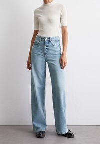 Ljusblå vida jeans med hög midja och synliga stygn, i kombination med en kortärmad krämfärgad ribbad topp. Slät textur, avslappnad design.