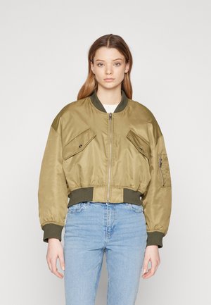 Maslinasto zeleni bomber jakna s sjajnim završetkom, oversized kroj, rebrasti manžeti i rub, te dva prednja džepa s preklopom.