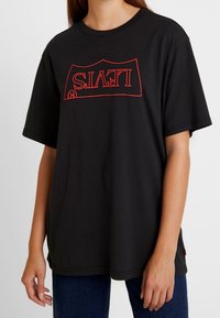 Camiseta de algodón negra con un logotipo rojo de Levi's en orientación invertida en el frente, con mangas cortas y un ajuste relajado.