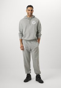 Sivá mikina s kapucňou a tepláky, s predným vreckom, kapucňou so šnúrkou a elastickým pásom. Čierne vysoké tenisky dopĺňajú look.