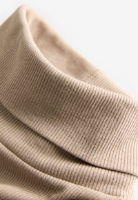 Beżowy, prążkowany golf o miękkiej fakturze. Materiał ozdobiony jest pionowymi paskami i ma gładkie, jednolite wykończenie.