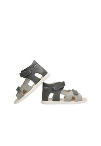 Dvě dvojice dětských sandálů v šedé a světle šedé kůži s suchými zipy, umístěné na bílém pozadí. Texturované podrážky.