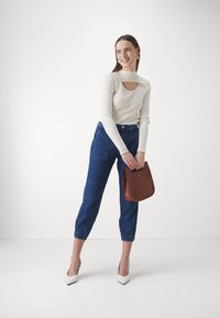 Top bianco a coste con scollatura, pantaloni cropped in denim blu con polsini elasticizzati e borsa marrone; modella con tacchi alti bianchi.