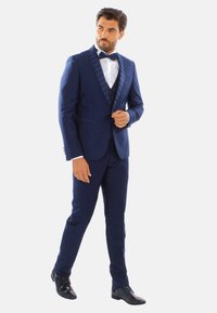 Tuxedo blu navy con colletto in satin a motivo, camicia bianca e papillon nero. Vestibilità sartoriale con scarpe nere eleganti.