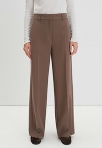 Braune weit geschnittene Hosen aus glattem Stoff, die über ein maßgeschneidertes Design mit flachem Bund und seitlichen Taschen verfügen.