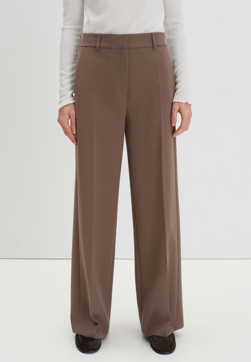 Braune weit geschnittene Hosen aus glattem Stoff, die über ein maßgeschneidertes Design mit flachem Bund und seitlichen Taschen verfügen.