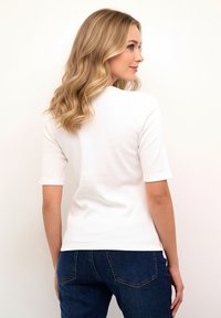 Tricou alb cu mânecă scurtă, striat, cu decolteu rotund, combinat cu blugi de culoare albastru închis, evidențiind un croi casual și o textură netedă.