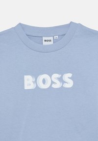 Ανοιχτό μπλε βαμβακερό μπλουζάκι με στρογγυλή λα ιμόκοψη. Διαθέτει τολμηρό, μερικώς σκιερό λευκό λογότυπο "BOSS" στο στήθος. Λεπτή υφή.