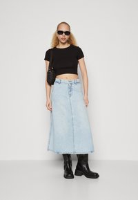 Svart avkortet t-skjorte, lyseblå denim maxiskjørt, svarte kne-høye støvler, liten svart veske, solbriller. Glatte teksturer, uformell design.