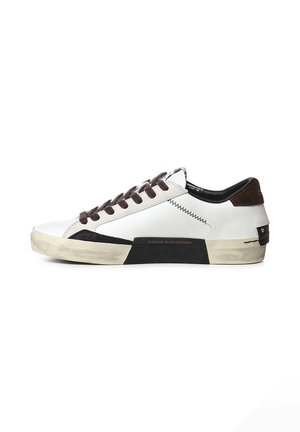 Sneaker bianco low-top con dettagli neri, lacci marroni e suola beige consumata, mostrato di lato su sfondo bianco.