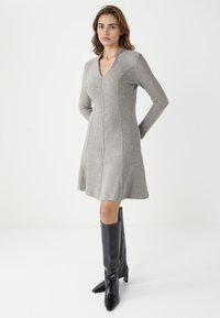 Grijze gebreide jurk met lange mouwen en een V-hals, voorzien van naaddetails. Gepaarde met zwarte knielange puntige laarzen.