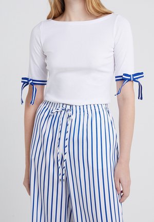 Biały krótki top z krótkim rękawem, ozdobiony niebiesko-białą wstążką z paskami przy rękawach, w zestawieniu z niebiesko-białymi pionowymi spodniami w paski. Lekki materiał.