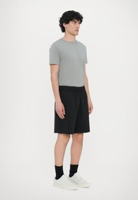 T-shirt grigia, pantaloni neri con elastico in vita, sneakers bianche, lunghezza media, tessuto morbido, vista laterale su uno sfondo neutro.