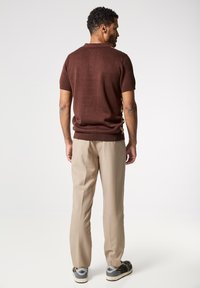 Polo marrón de manga corta con un acabado texturizado, combinado con pantalones beige claros y zapatillas grises con acentos negros.