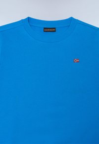 T-shirt in cotone blu con collo rotondo a costine. Presenta un piccolo logo ricamato della bandiera norvegese sul petto. Texture liscia.