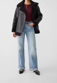 Czarna kurtka z materiału skóropodobnego z barankowym wykończeniem, w zestawieniu z jasnoniebieskimi spodniami typu wide-leg i czarnymi, szpiczastymi balerinami. Prosty design.