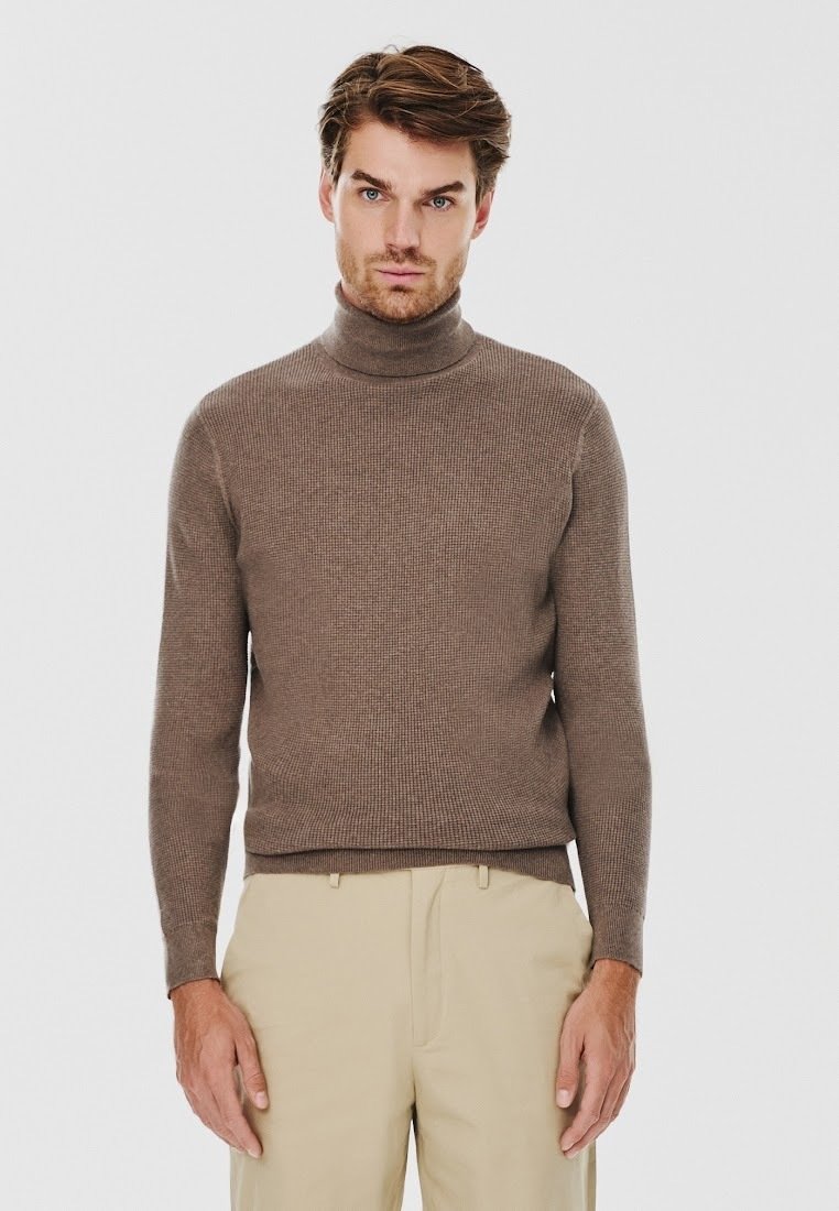 Brązowy sweter z wysokim kołnierzem, prążkowany, wykonany z dzianiny, z długimi rękawami, zestawiony z beżowymi spodniami. Prosty i dopasowany design.