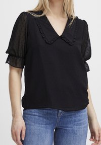Sort bluse med puffede ærmer, bølget krave og tekstureret stof, parret med lyseblå denim jeans. Glat og let materiale.