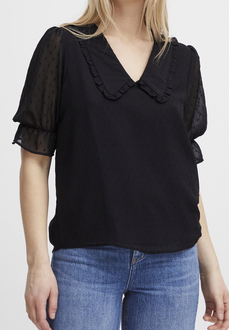 Sort bluse med puffede ærmer, bølget krave og tekstureret stof, parret med lyseblå denim jeans. Glat og let materiale.