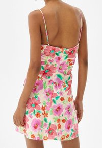 Vestido floral con un fondo en tonos pastel y flores vibrantes en rosa y rojo, tirantes finos y un diseño ajustado con cierre en la parte posterior.