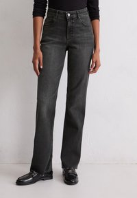 Jeans en denim noir taille haute avec une coupe droite, présentant des poches avant, des coutures contrastées et un détail zippé à l'ourlet.
