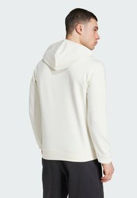 Weißer Kapuzenpullover mit weicher Textur, ausgestattet mit einer Kängurutasche und gerippten Bündchen. Das Design ist schlicht und unaufdringlich.